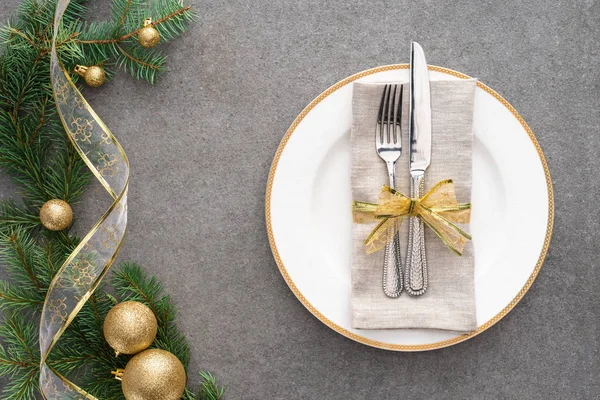 Vista sopraelevata del tavolo servito con piatto, forchetta e coltello avvolto da nastro festivo vicino al ramo decorato da palline di Natale dorate — Foto stock