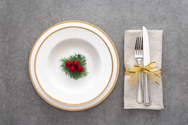 Vista de cima da placa servida com galho evergreen decorado e bolas de Natal perto de garfo com faca enrolada por fita na superfície cinza — Fotografia de Stock