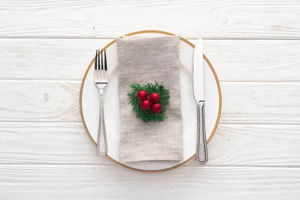 Возвышенный вид подаваемой тарелки с вилкой, ножом и украшенной вечнозеленой веткой с рождественскими шариками на деревянном столе — стоковое фото