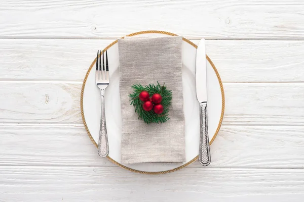 Vista elevada da placa servida com garfo, faca e ramo evergreen decorado com bolas de Natal na mesa de madeira — Fotografia de Stock