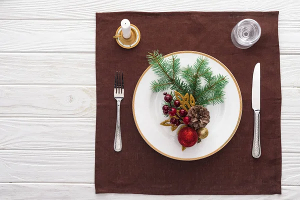 Vista dall'alto del tavolo servito con bicchiere da vino, piatto, forchetta, coltello, cucchiaio, candela e decorazioni natalizie sulla tovaglia — Foto stock