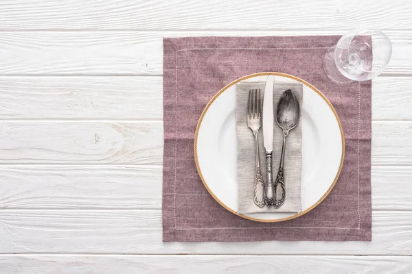 Flat lay with plate, fork, knife, spoon near wine glass on served table with table cloth — Stock Photo