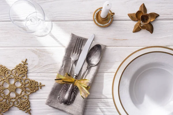Vista superior de vidro de vinho, prato com bolas de Natal douradas, vela e garfo, colher, faca enrolada por fita na mesa de madeira — Fotografia de Stock