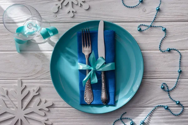 View from above of wine glass, decorated snowflakes and beads, plate with fork and knife wrapped by ribbon on wooden table — Stock Photo