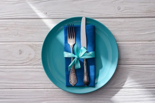 Flat lay with fork and knife wrapped by festive ribbon on plate on wooden table — Stock Photo