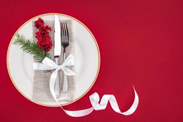 Vista dall'alto di piatto con ramo di pino, bacche, forchetta e coltello avvolto da nastro su piatto isolato su rosso — Foto stock