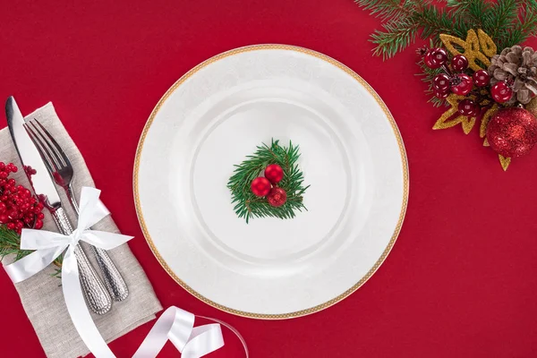 Vista desde arriba de tenedor, cuchillo, bayas rojas envueltas en cinta y decoraciones navideñas aisladas en rojo — Stock Photo