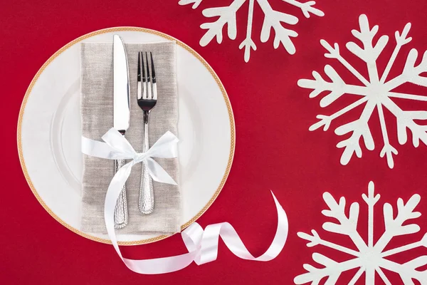 Elevated view of plate with fork and knife wrapped by festive ribbon on plate surrounded by snowflakes isolated on red — Stock Photo