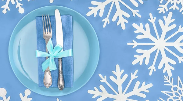 Vue de dessus de la fourchette et du couteau enveloppés par un ruban festif sur une assiette entourée de flocons de neige isolés sur du bleu — Photo de stock