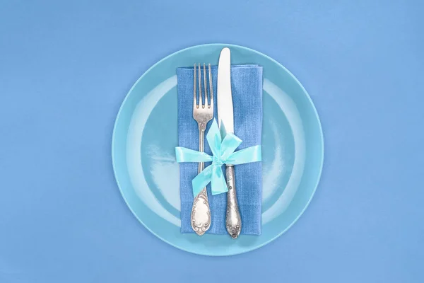 Плоский лежав з виделкою і ножем, загорнутий святковою стрічкою на тарілці ізольований на синьому — стокове фото