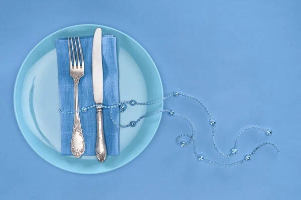 View from above of fork and knife wrapped by festive beads on plate isolated on blue — Stock Photo