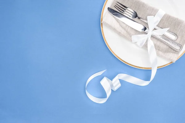 Elevated view of fork and knife wrapped by festive ribbon on plate isolated on blue — Stock Photo