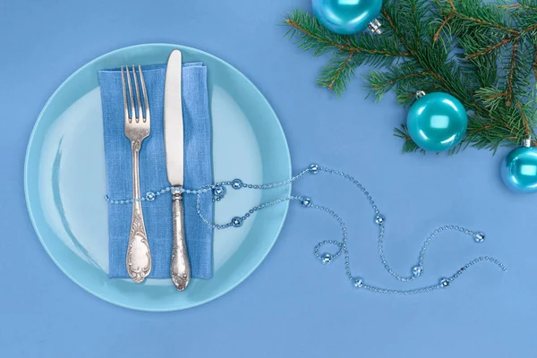 View from above of fork and knife wrapped by beads on plate near evergreen branches with christmas balls isolated on blue — Stock Photo