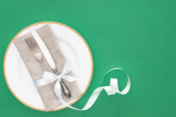 Vista elevada de la placa con tenedor y cuchillo envuelto por cinta festiva aislada en verde - foto de stock
