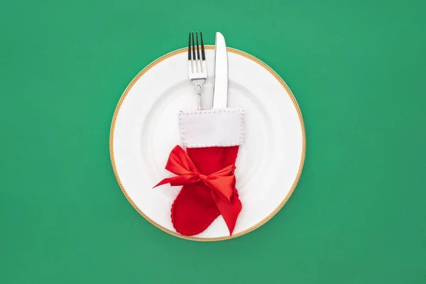 Top view of fork and knife in christmas sock on plate isolated on green — Stock Photo