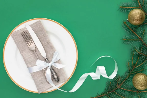 Flat lay with fork and knife wrapped by festive ribbon on plate near evergreen tree branches with christmas balls isolated on blue — Stock Photo