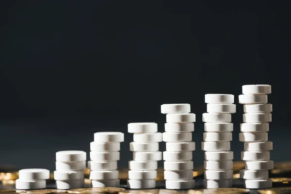 Close up view of arranged stacks made of white pills near pile of coins on grey — Stock Photo