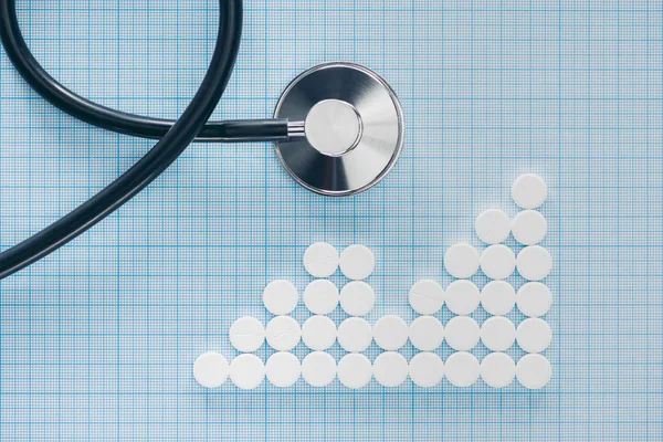 View from above of stethoscope and arranged white pills on blue checkered surface — Stock Photo