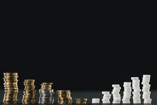 Arranged stacks made of white pills and coins placed in rows on black — Stock Photo