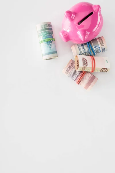 Top view of pink piggy bank and various rolled russian banknotes on white surface — Stock Photo