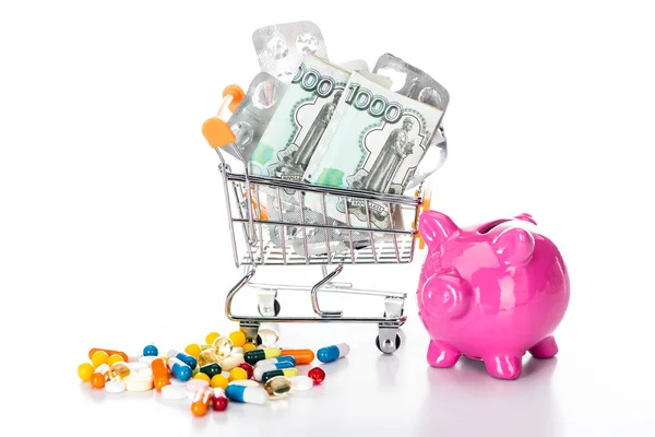 Close up shot of trolley cart with russian cash money and empty pills packages near pink piggy bank and colorful pills isolated on white — Stock Photo