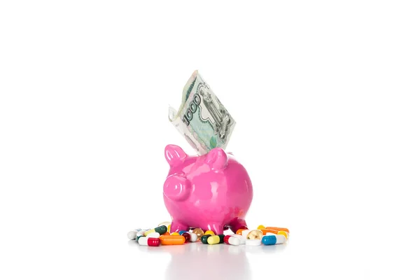 Pink piggy bank with russian banknote surrounded by various colorful pills isolated on white — Stock Photo