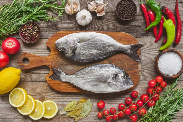 Top view of raw fish on wooden board surrounded by ingredients on table — Stock Photo