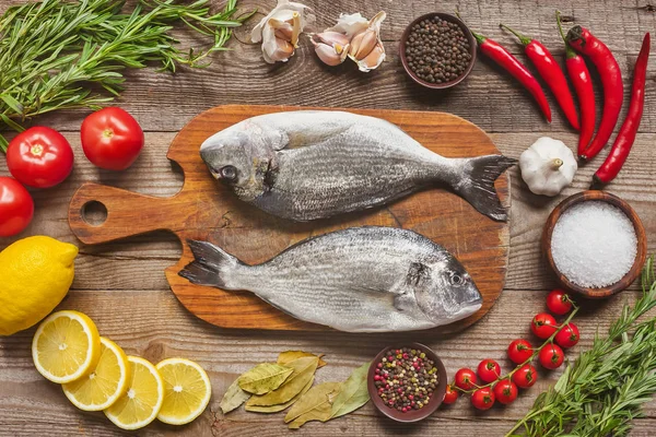 Food composition with raw fish on wooden board surrounded by ingredients on table — Stock Photo