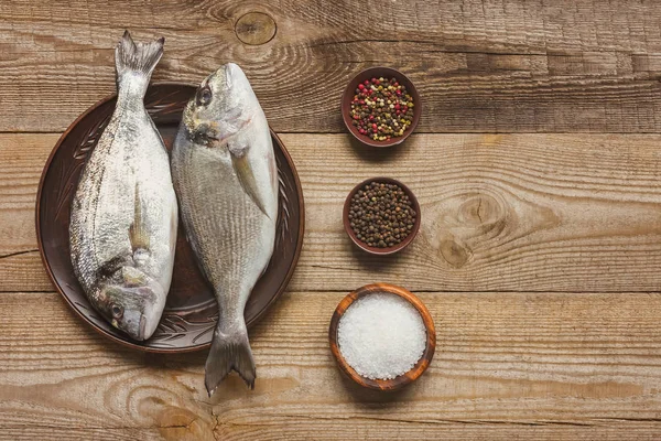 Vista elevada de sal, pimenta e prato com peixe não cozido na mesa de madeira — Fotografia de Stock