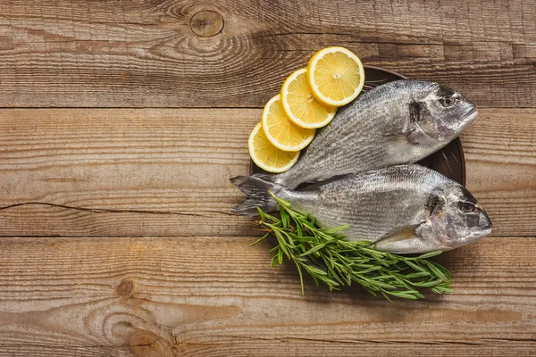 Vista superior de peixe cru com limão e alecrim em mesa de madeira — Fotografia de Stock