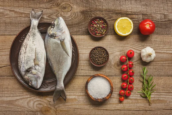 Vista sopraelevata del piatto con pesce crudo vicino agli ingredienti disposti sul tavolo di legno — Foto stock