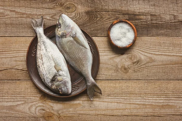 Top view of salt and plate with uncooked fish on wooden table — Stock Photo