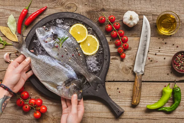 Partial view of tattooed man putting uncooked fish on tray — Stock Photo