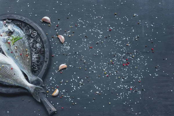 Vista sopraelevata di pesce crudo con rosmarino in vassoio su tavolo nero con aglio — Foto stock