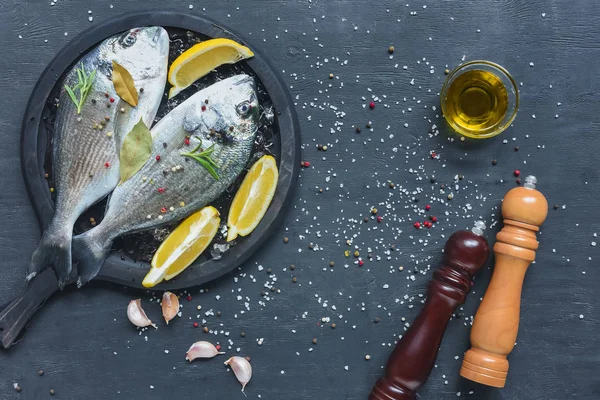Composición de alimentos con pescado crudo en bandeja sobre mesa negra con ingredientes - foto de stock