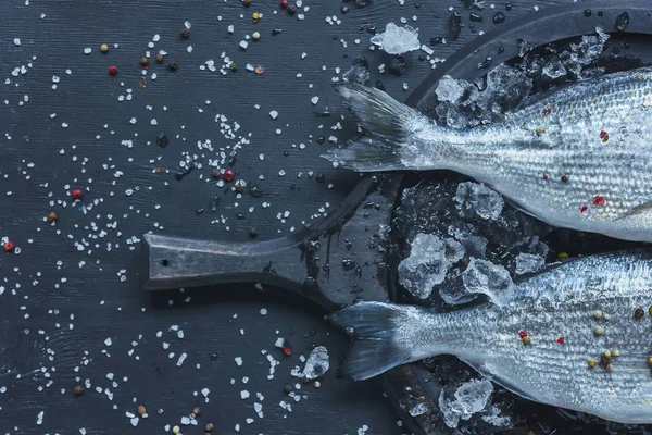 Top view of raw fish in tray on black table covered by salt and pepper — Stock Photo