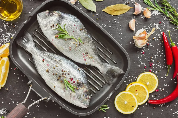 Erhöhte Ansicht von rohem Fisch im Backblech, umgeben von Zutaten auf schwarzem Tisch — Stockfoto