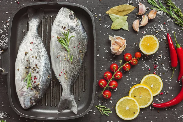 Erhöhte Ansicht von rohem Fisch in der Nähe von Zutaten auf schwarzem Tisch — Stockfoto