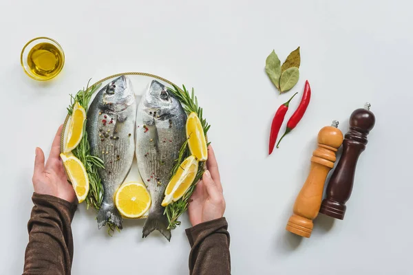 Vista parcial de la mujer tomando plato con pescado decorado con romero y limón - foto de stock