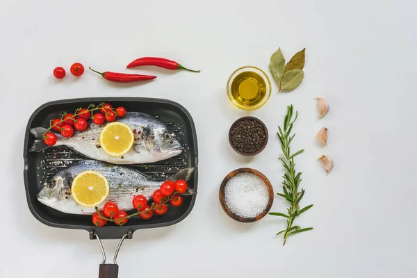 Vista elevada de ingredientes, peixes não cozidos decorados com tomate limão e cereja em assadeira na mesa branca — Fotografia de Stock