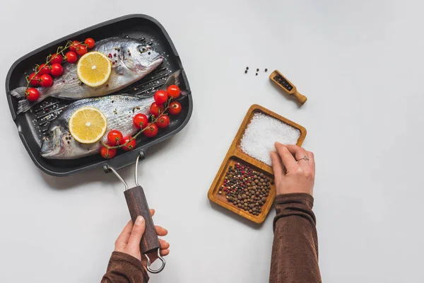 Cropped image of woman taking salt at table with uncooked fish and ingredients in tray — Stock Photo