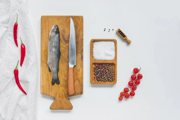 Flat lay com faca e peixe não cozido em tábua de madeira perto de ingredientes na mesa branca — Fotografia de Stock