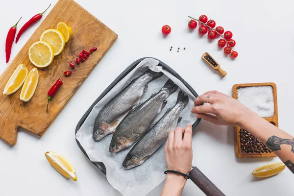 Immagine ritagliata di donna che mette pesce crudo in vassoio con carta da forno su tavolo bianco con ingredienti — Foto stock