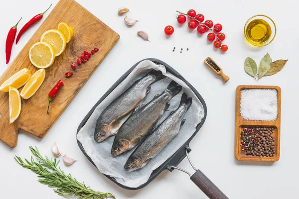 Vue du dessus du poisson dans une plaque de cuisson entourée de divers ingrédients sur une table blanche — Photo de stock