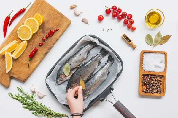 Imagem cortada de mulher colocando folha de louro em peixes não cozidos em assadeira na mesa com ingredientes — Fotografia de Stock