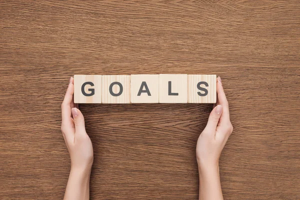 Partial view of person holding 'goals' word made of wooden blocks on wooden tabletop, goal setting concept — Stock Photo