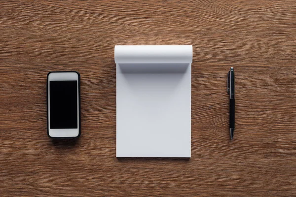 Vue du haut du stylo, ordinateur portable avec espace de copie et smartphone avec écran blanc sur fond en bois — Photo de stock