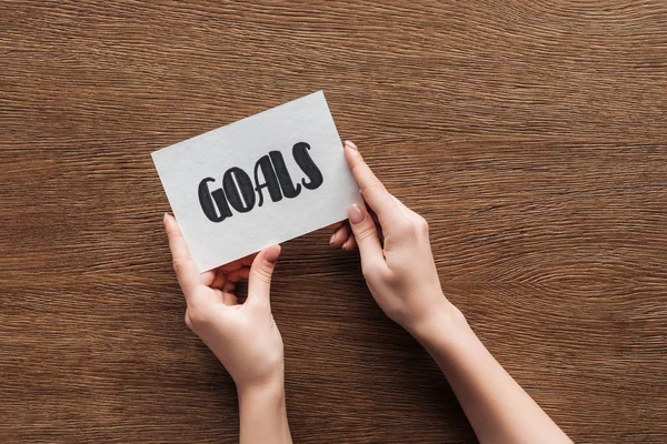 Cropped view of woman holding card with 'goals' lettering in hands on wooden background — Stock Photo