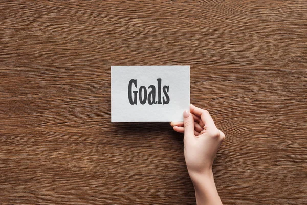 Cropped view of woman holding 'goals' lettering on card in hand on wooden background — Stock Photo