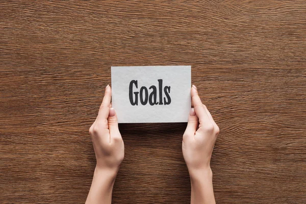 Cropped view of woman holding card with 'goals' lettering in hands on wooden background — Stock Photo